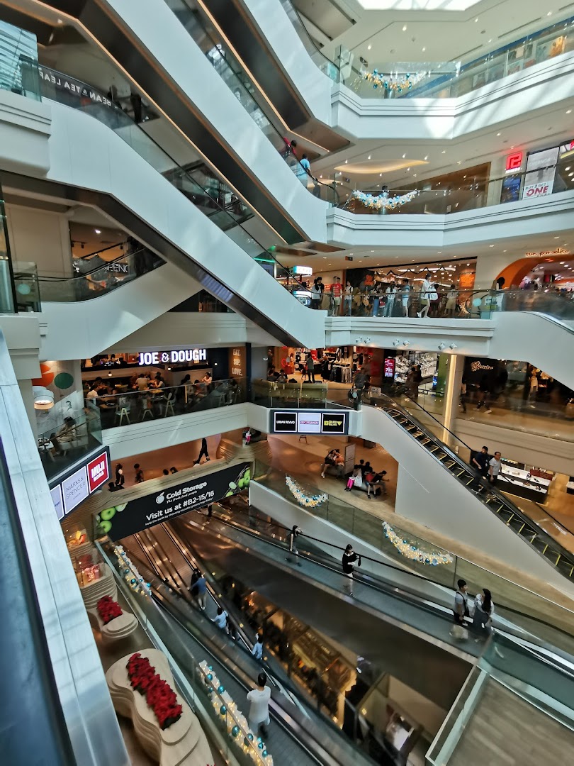 A bustling multi-level shopping mall interior featuring escalators, various shops, and numerous visitors.