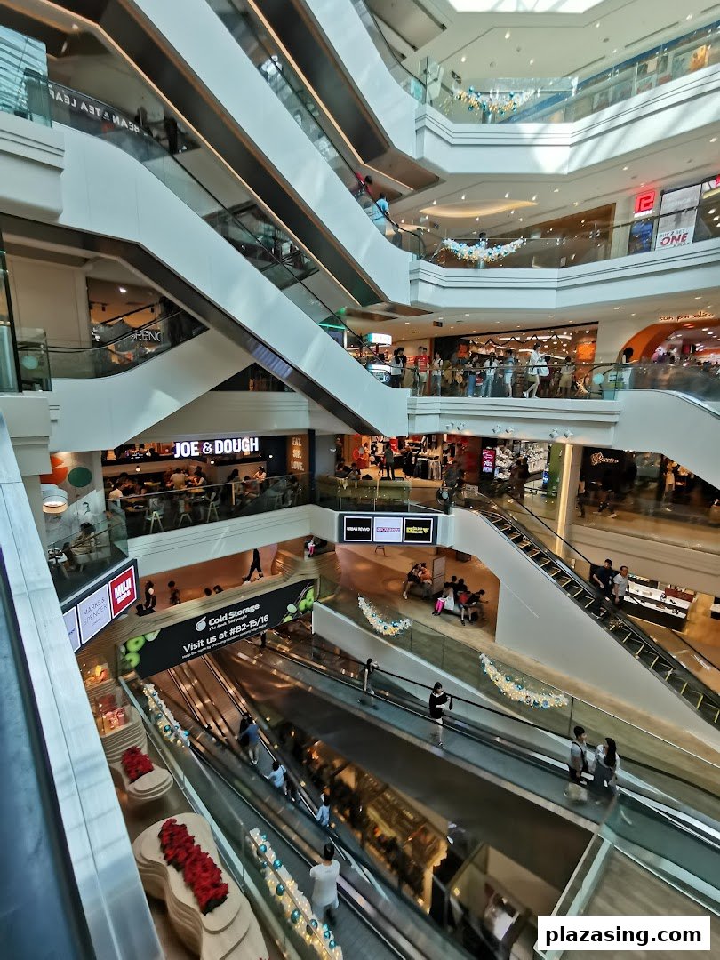 A bustling multi-level shopping mall interior featuring escalators, various shops, and numerous visitors.