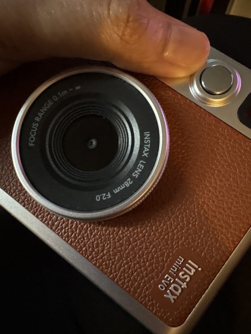 Close-up of a hand holding a stylish brown Instax Mini Evo instant camera.