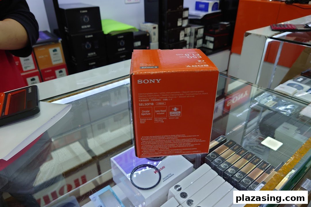 A Sony camera lens box displayed on a glass counter in an electronics store.