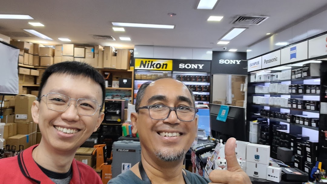 Two smiling men in a well-stocked electronics and camera shop featuring major brands.