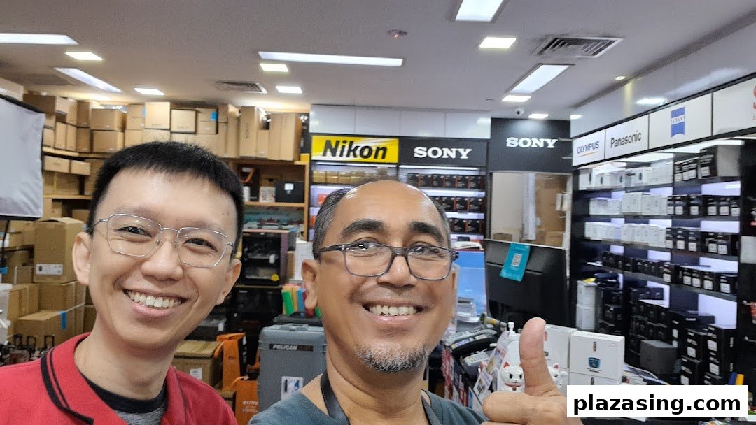 Two smiling men in a well-stocked electronics and camera shop featuring major brands.