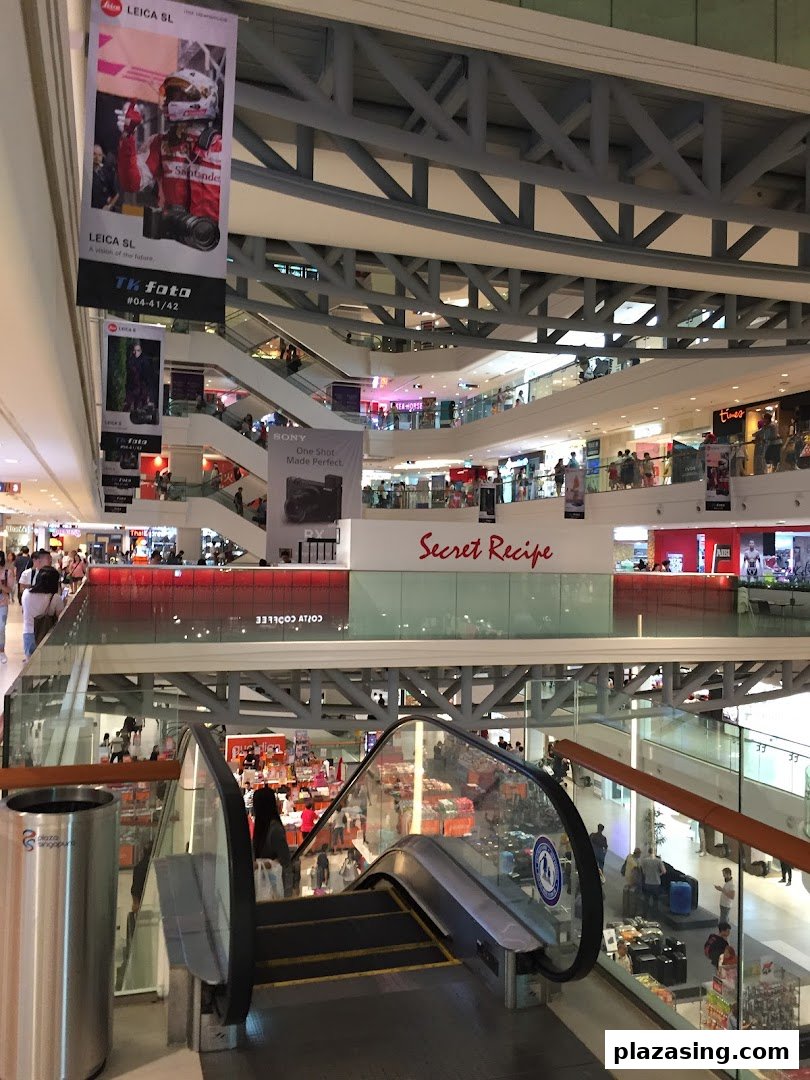A vibrant multi-level shopping mall interior with escalators, various shops, and bustling activity.