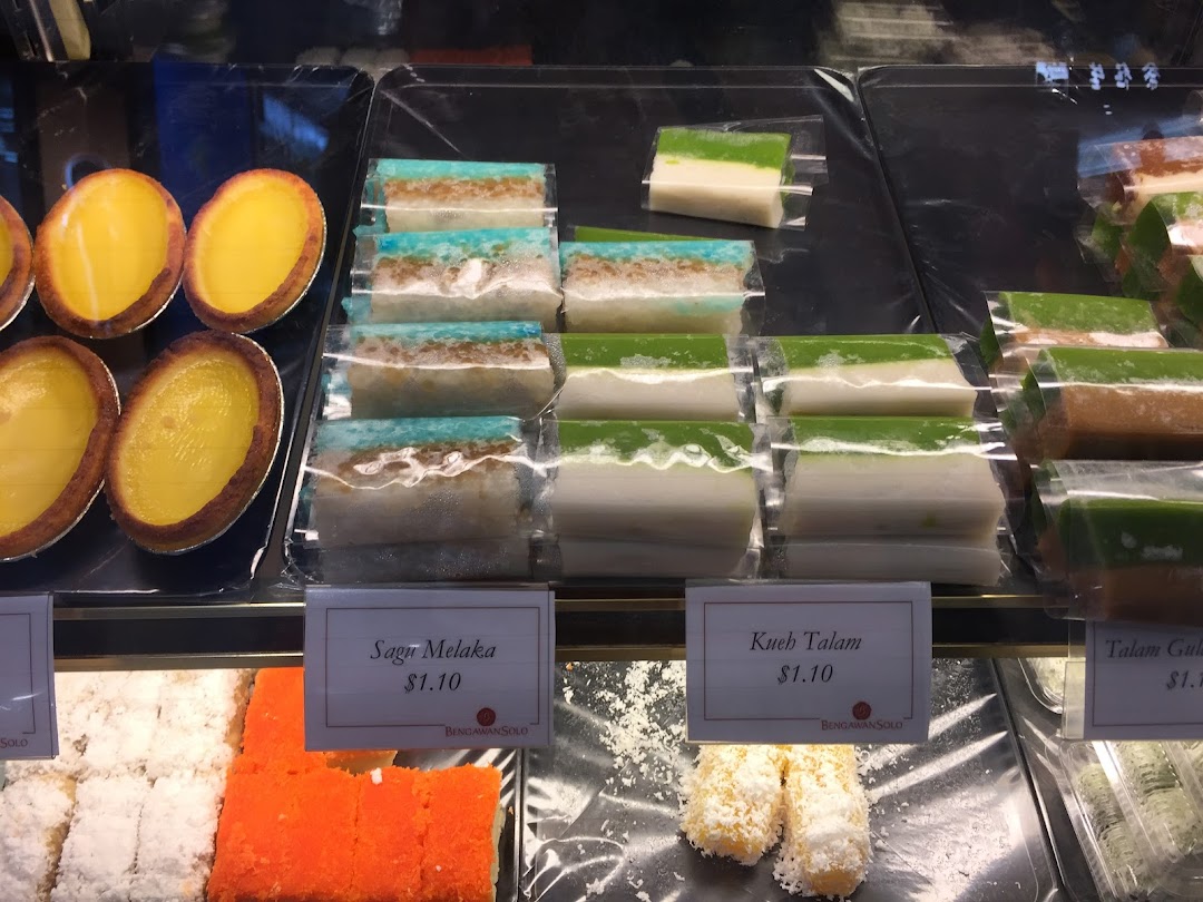 A vibrant display of traditional Indonesian kueh and egg tarts in a retail shop's glass case.
