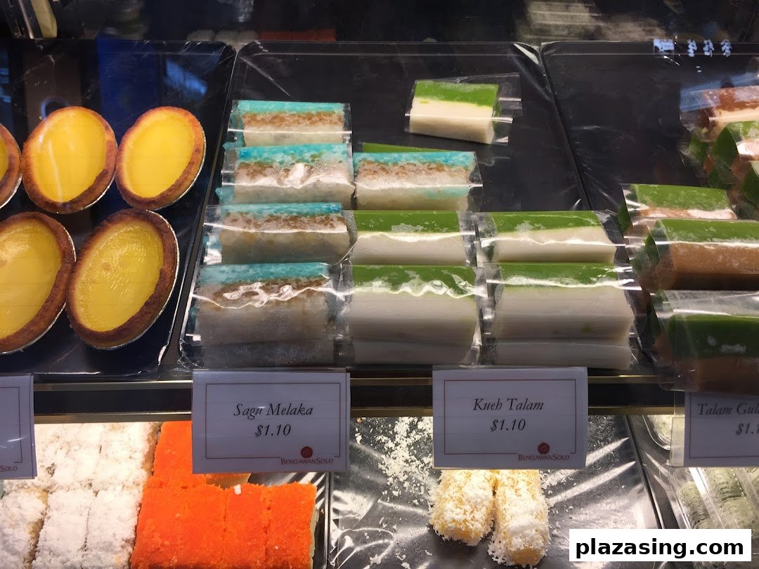 A vibrant display of traditional Indonesian kueh and egg tarts in a retail shop's glass case.