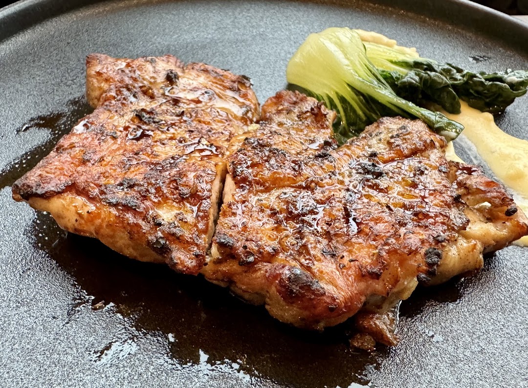 A perfectly grilled chicken or pork dish with bok choy and creamy sauce on a dark plate.