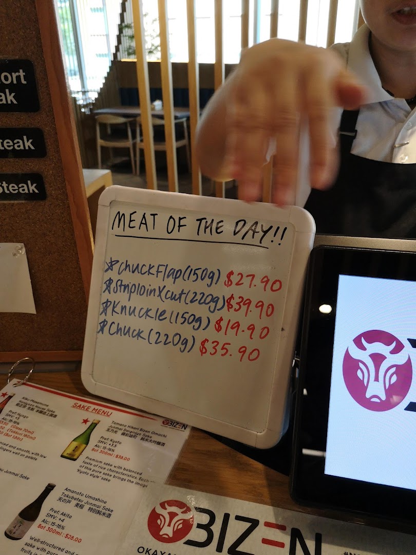 A whiteboard displaying 'Meat of the Day' specials and a partial sake menu at Bizen Wagyu Salad Bar.