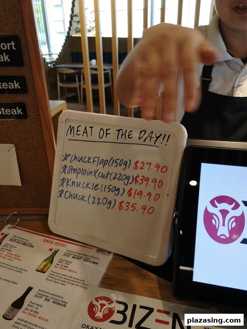 A whiteboard displaying 'Meat of the Day' specials and a partial sake menu at Bizen Wagyu Salad Bar.
