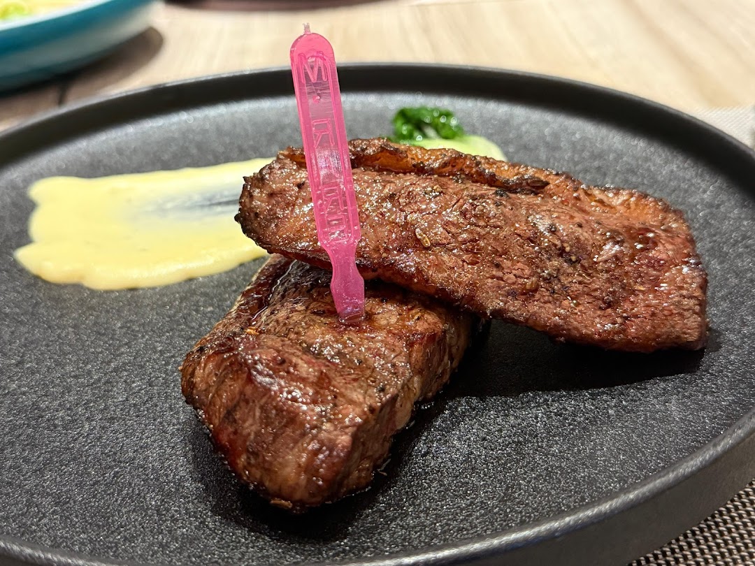 A perfectly cooked steak served on a dark plate with a side of mashed potatoes and a pink pick.