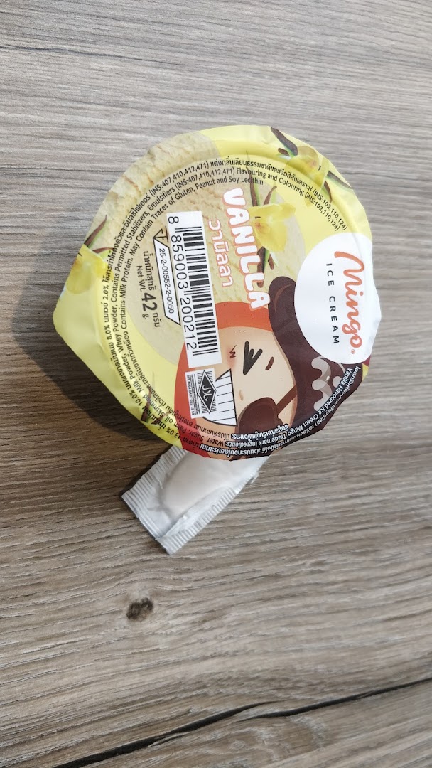 A Mingo vanilla ice cream cup with a small spoon, resting on a wooden surface.