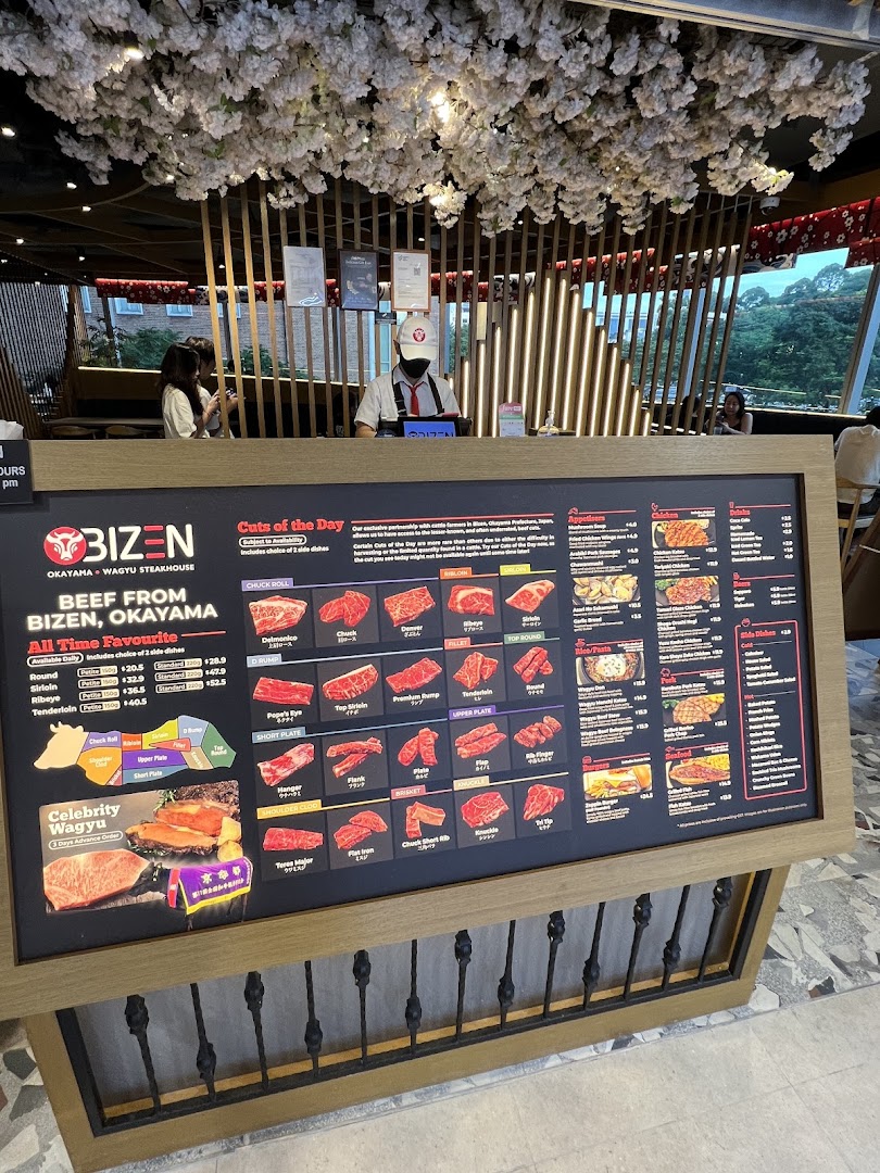 A large menu board at Bizen Wagyu Steakhouse entrance, showcasing premium beef cuts and other dishes, with a staff member.