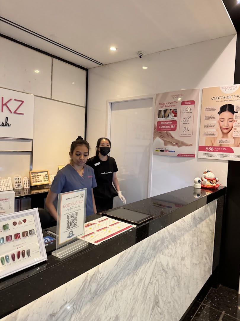 Two staff members at the BodyWerkz reception desk, with promotional posters for beauty treatments and nail samples visible.