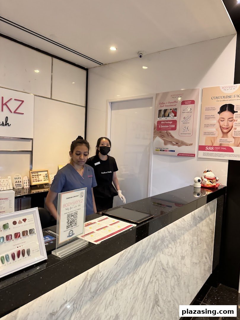 Two staff members at the BodyWerkz reception desk, with promotional posters for beauty treatments and nail samples visible.