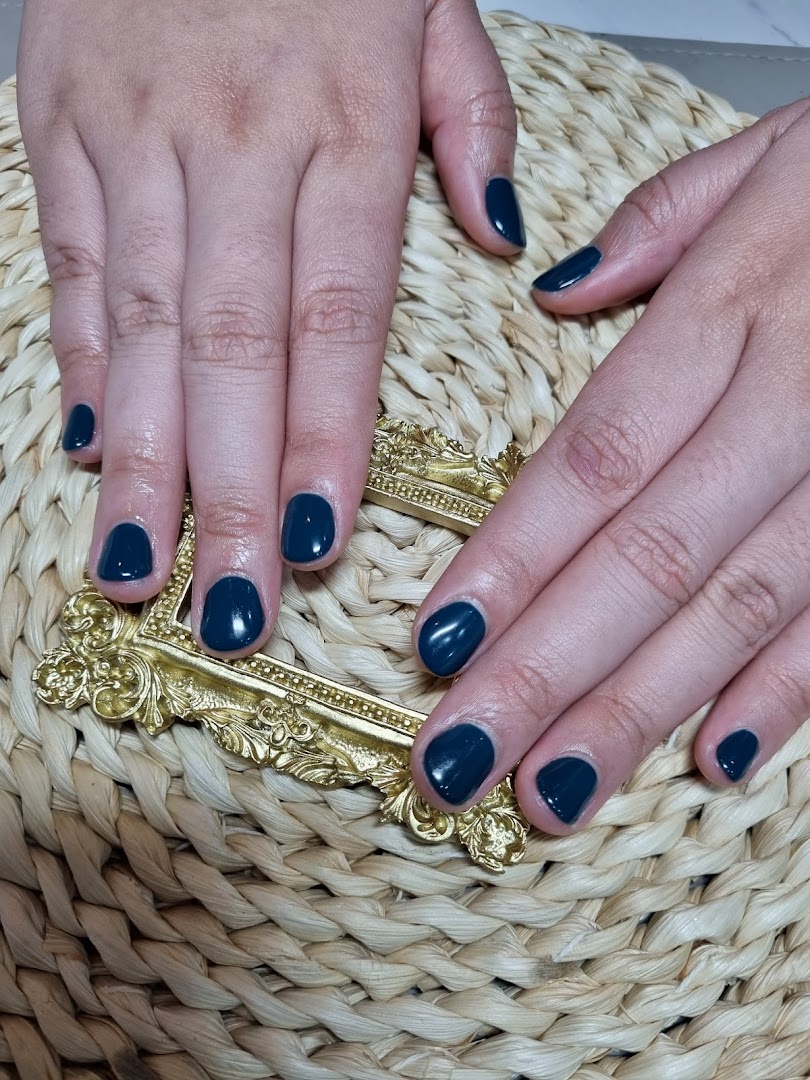 Close-up of hands showcasing a fresh dark teal manicure on a woven surface with a gold accent.