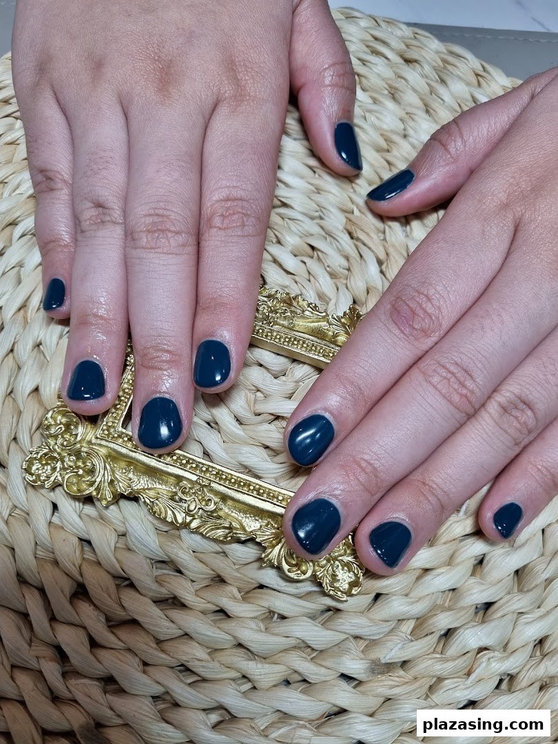 Close-up of hands showcasing a fresh dark teal manicure on a woven surface with a gold accent.