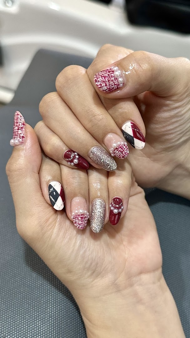 Close-up of a hand showcasing intricate nail art with tweed, glitter, and pearl designs.