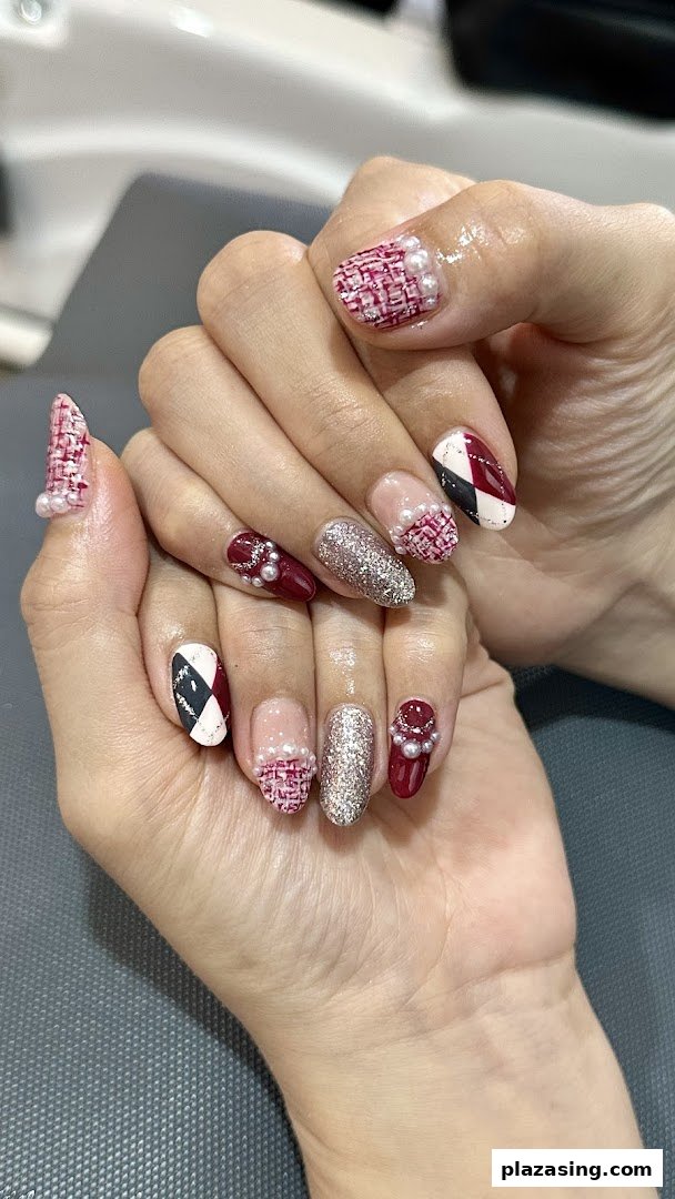 Close-up of a hand showcasing intricate nail art with tweed, glitter, and pearl designs.