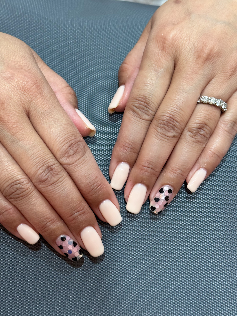 Close-up of hands showcasing a fresh manicure with nude polish and heart-shaped glitter accents.