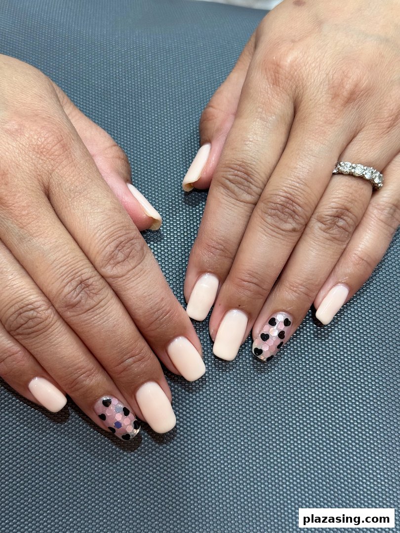 Close-up of hands showcasing a fresh manicure with nude polish and heart-shaped glitter accents.