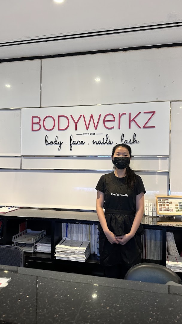 A friendly staff member stands at the reception desk of BodyWerkz, a beauty salon.