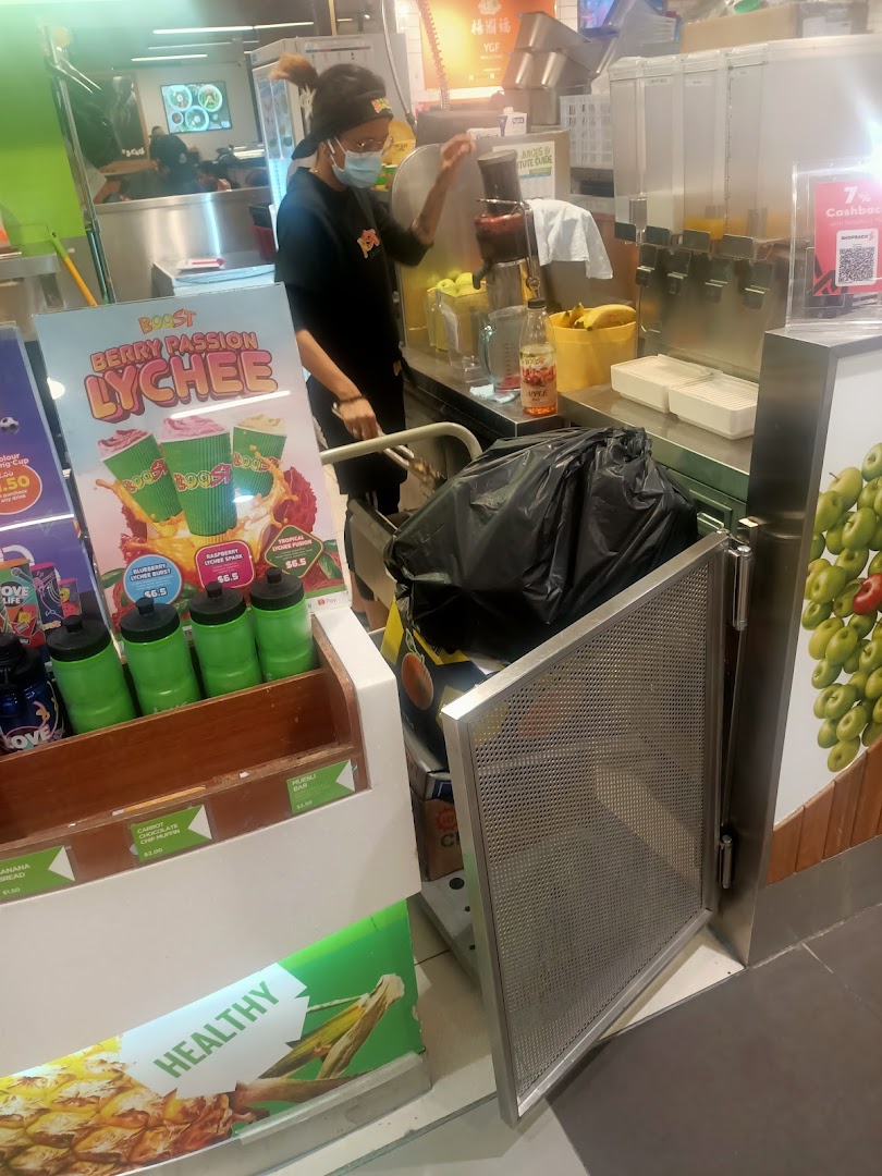 An employee at Boost Juice prepares a fresh drink, with promotional displays for Berry Passion Lychee and healthy snacks.