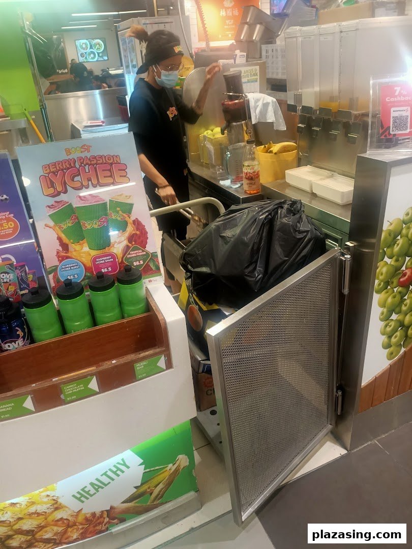 An employee at Boost Juice prepares a fresh drink, with promotional displays for Berry Passion Lychee and healthy snacks.