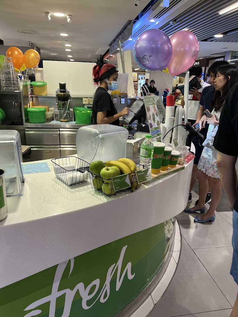 A Boost Juice staff member serves customers at the counter, with fresh fruit displayed.