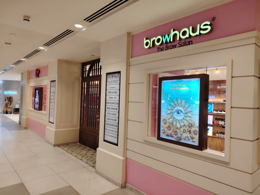 The inviting pink and white shopfront of Browhaus, 'The Brow Salon,' featuring its entrance and a promotional display.