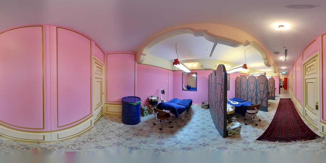 A vibrant pink and gold interior of Browhaus, featuring treatment beds, privacy screens, and a hallway.