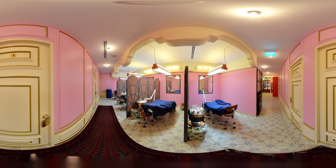 A vibrant pink and gold interior of Browhaus, featuring multiple treatment stations with beds and beauty equipment.