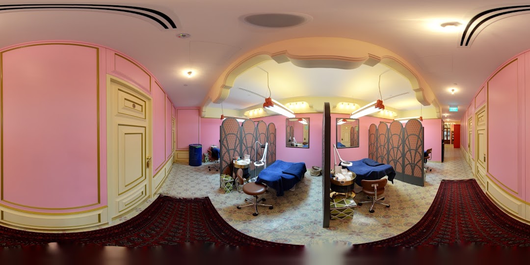 A vibrant pink and gold interior of Browhaus, featuring multiple treatment stations with privacy screens and elegant decor.