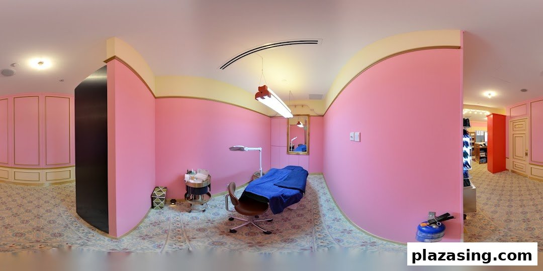 A pink-walled treatment room with a bed, chair, and beauty equipment, featuring ornate flooring.