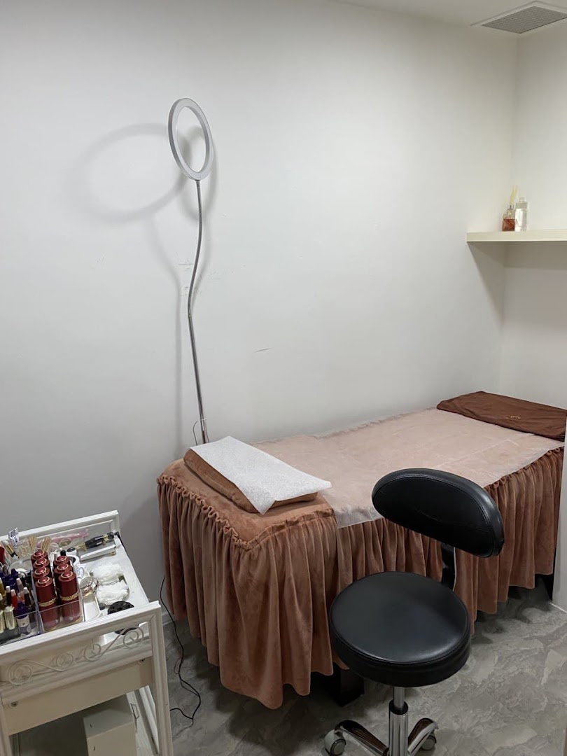 A clean and well-equipped treatment room for eyebrow embroidery services, featuring a bed, stool, and supplies.