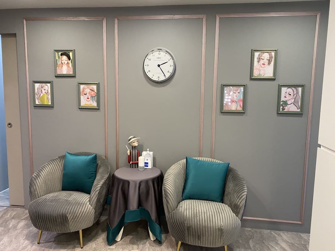 A cozy and stylish waiting area featuring two plush armchairs, a small table, and framed art on a grey wall.