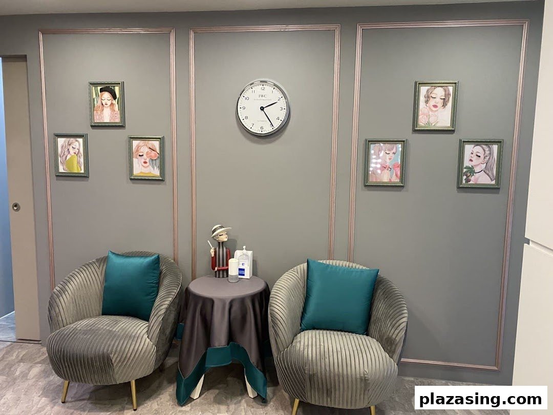 A cozy and stylish waiting area featuring two plush armchairs, a small table, and framed art on a grey wall.