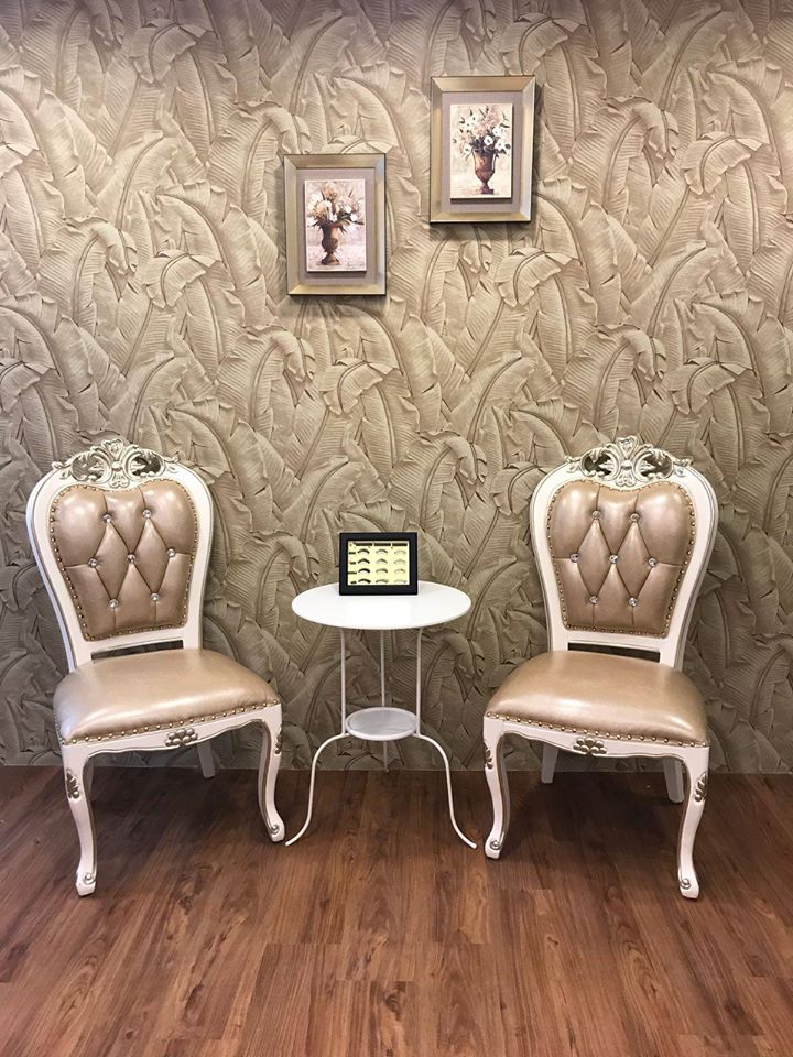 Two ornate chairs and a small table in a waiting area with leaf-patterned wallpaper and framed art.