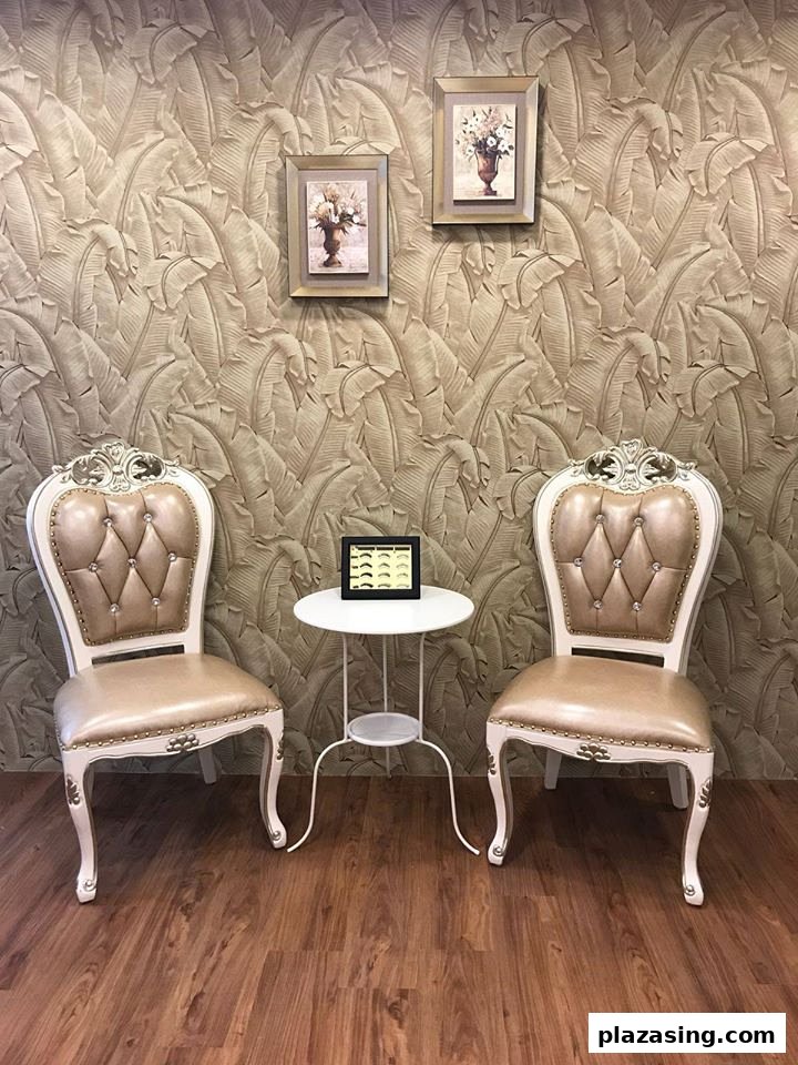 Two ornate chairs and a small table in a waiting area with leaf-patterned wallpaper and framed art.
