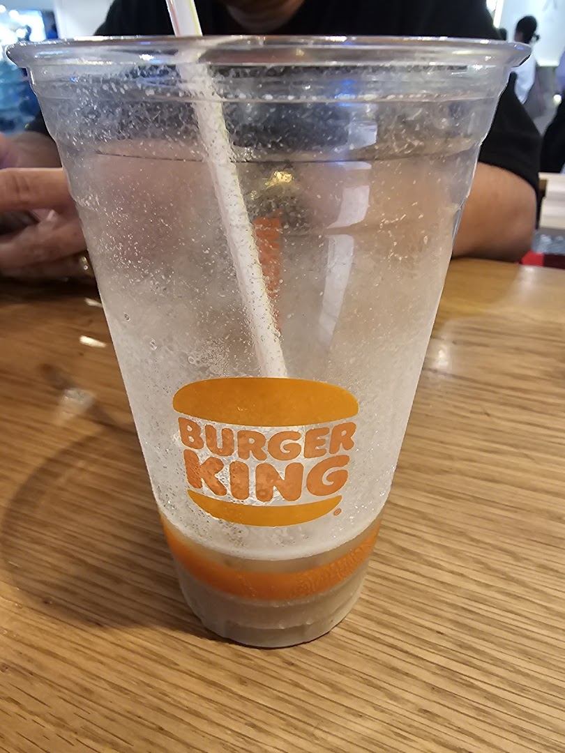 A clear plastic Burger King cup with a straw, partially filled, on a wooden table.