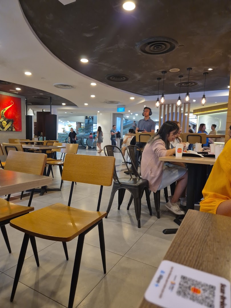 Diners enjoying meals inside Burger King, with modern seating and mall activity visible in the background.