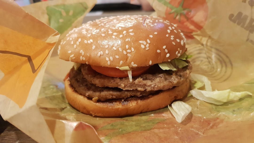 A close-up of a double patty burger with lettuce and tomato in Burger King wrapping.