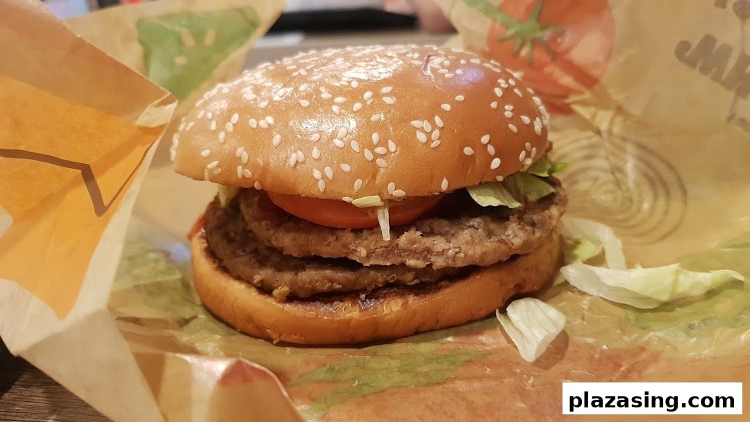 A close-up of a double patty burger with lettuce and tomato in Burger King wrapping.