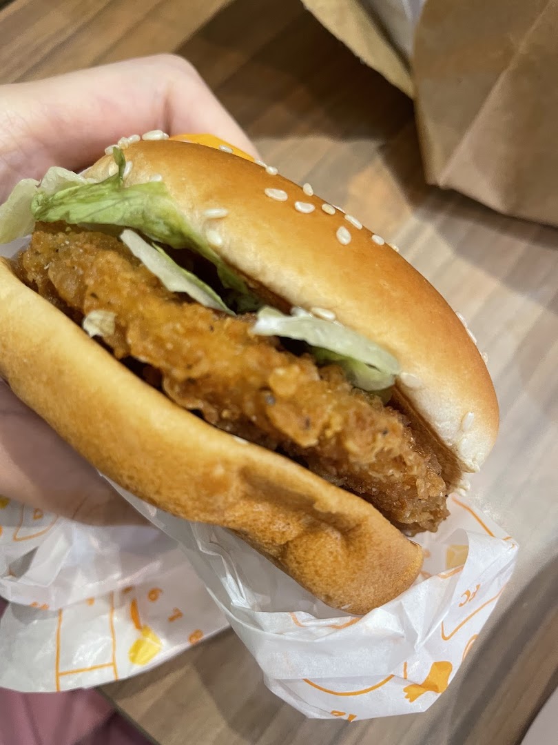 A hand holds a delicious-looking crispy chicken burger with lettuce and cheese.
