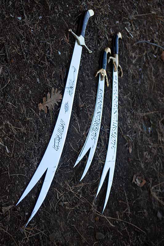 Three ornate swords with Arabic calligraphy and unique split blades lie on dark ground.