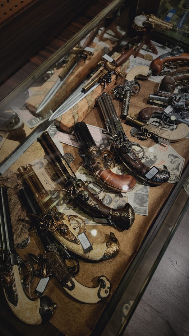A close-up view of a display case showcasing ornate antique-style pistols, daggers, and historical artifacts.