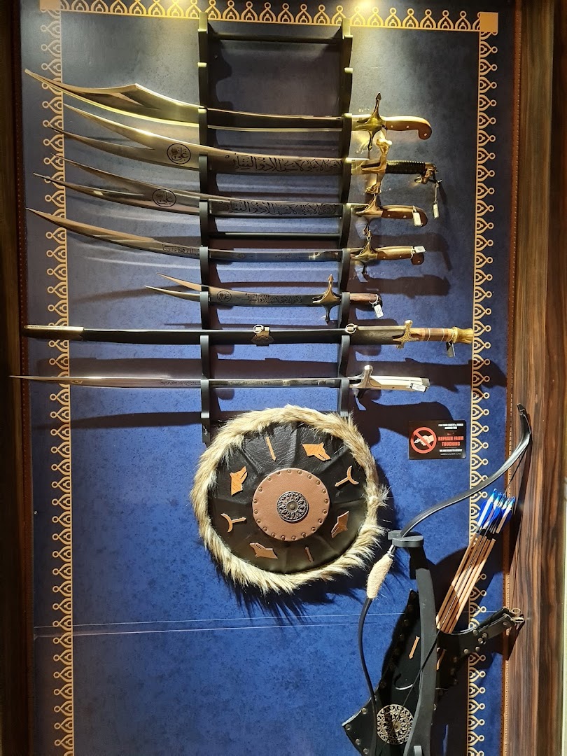 A display of ornate swords, a fur-trimmed shield, and a bow with arrows on a blue wall.