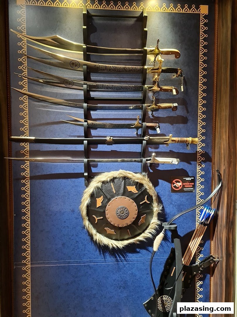 A display of ornate swords, a fur-trimmed shield, and a bow with arrows on a blue wall.