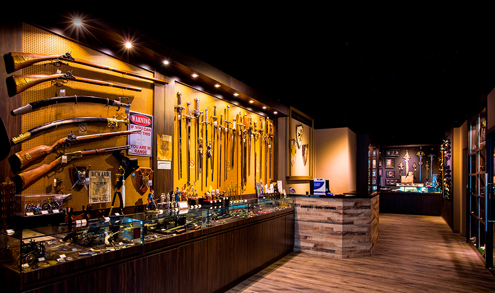 Interior view of a shop displaying an extensive collection of historical swords, firearms, and armour.
