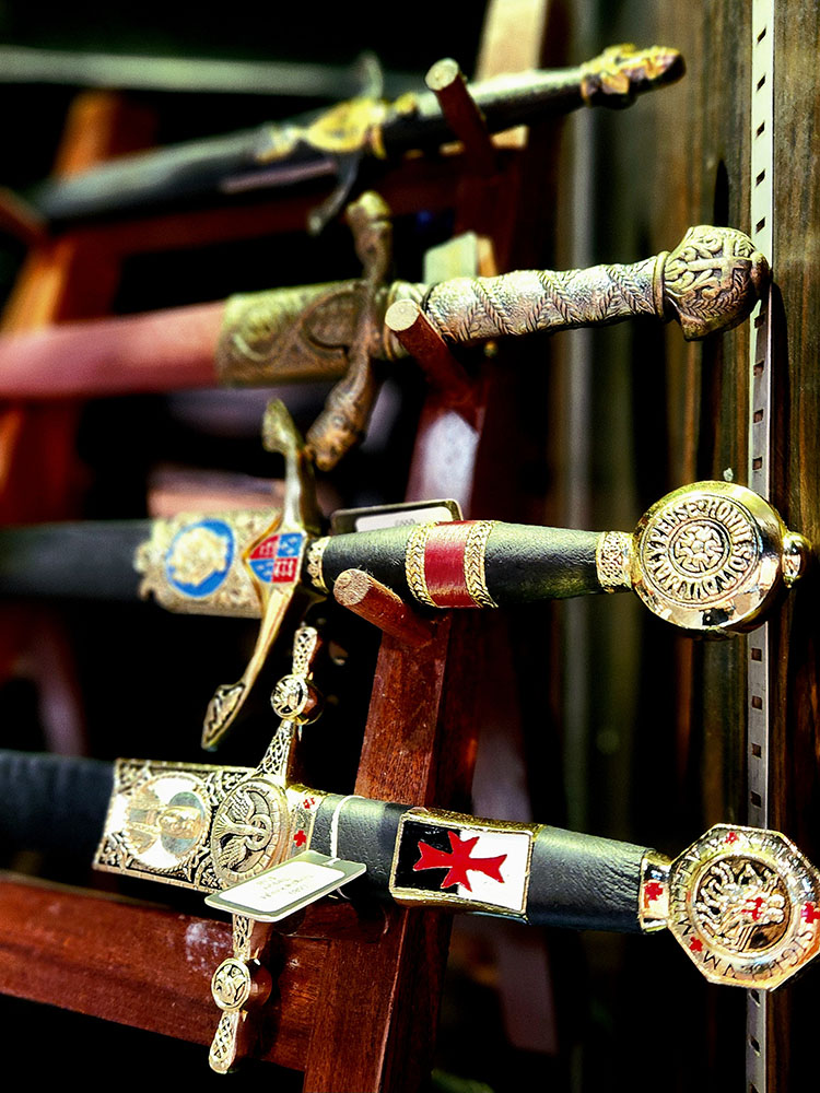 A close-up view of several ornate, historical-style swords displayed on a wooden rack, showcasing intricate hilts and scabbards.