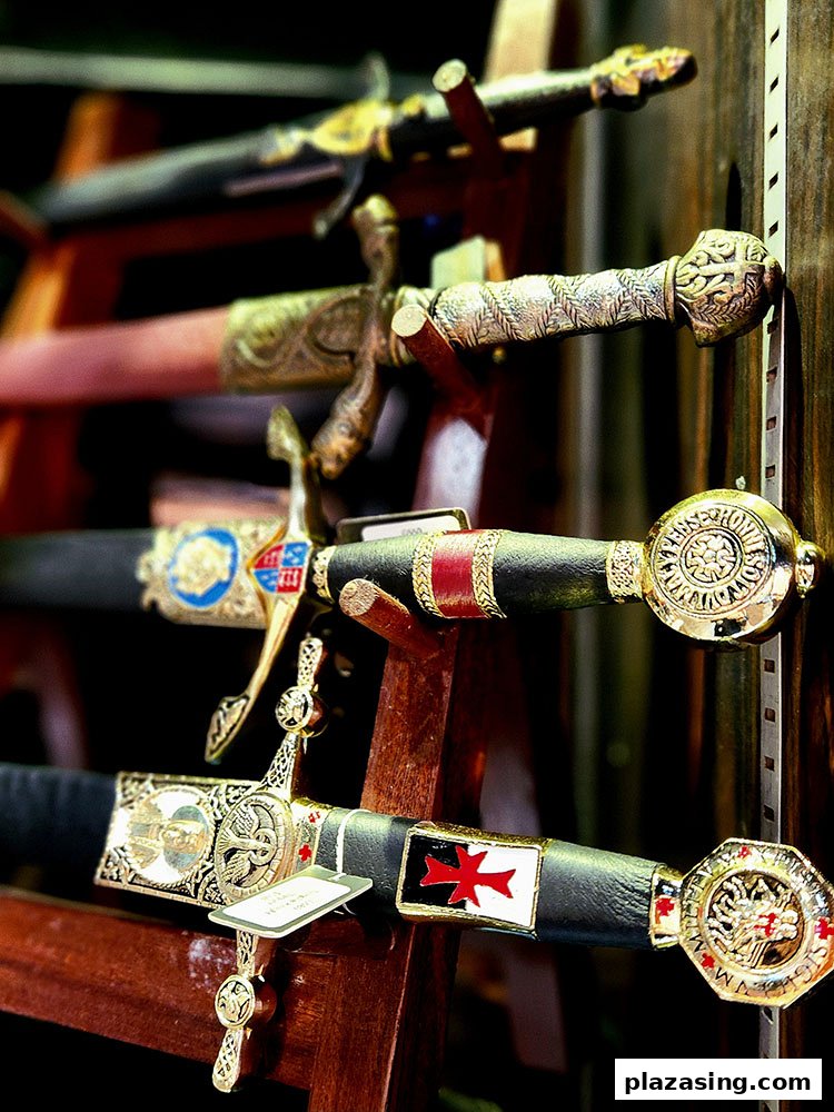 A close-up view of several ornate, historical-style swords displayed on a wooden rack, showcasing intricate hilts and scabbards.