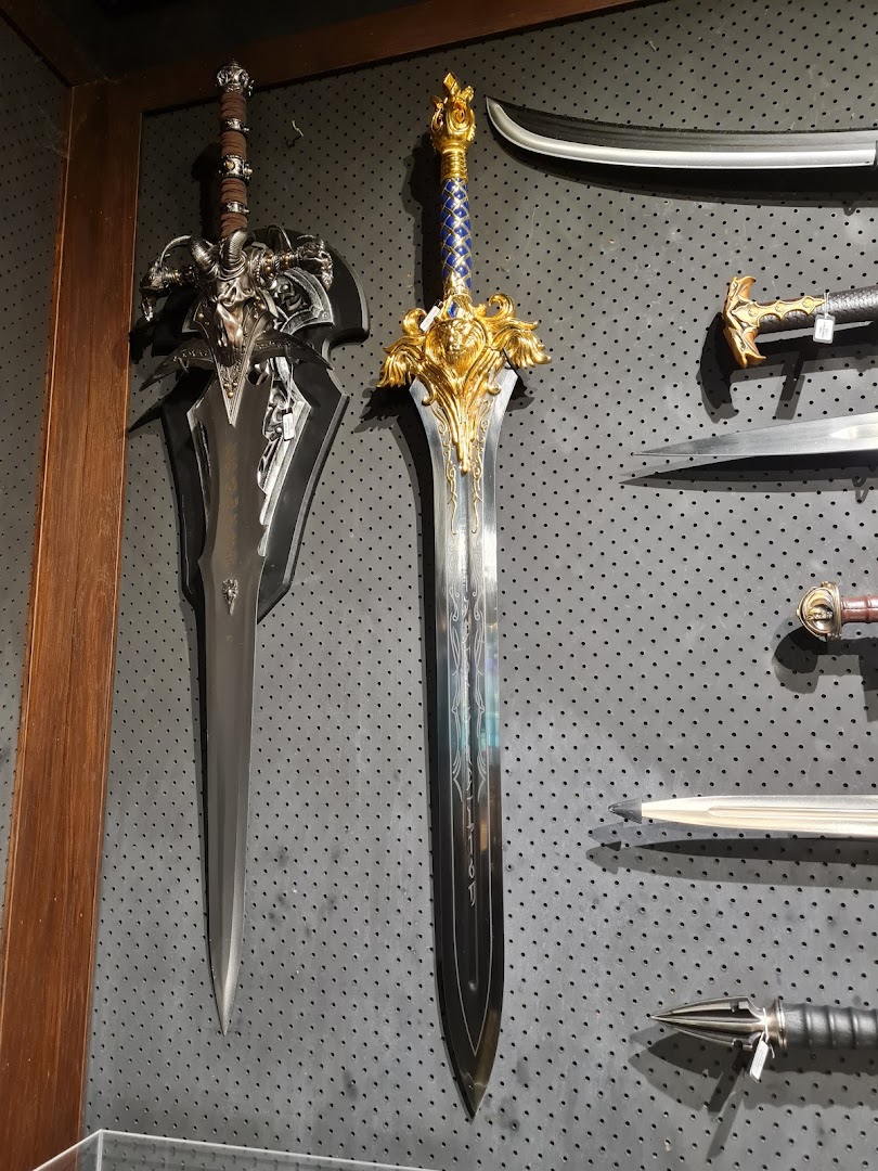 A display of ornate, fantasy-style swords and bladed weapons on a dark pegboard wall.